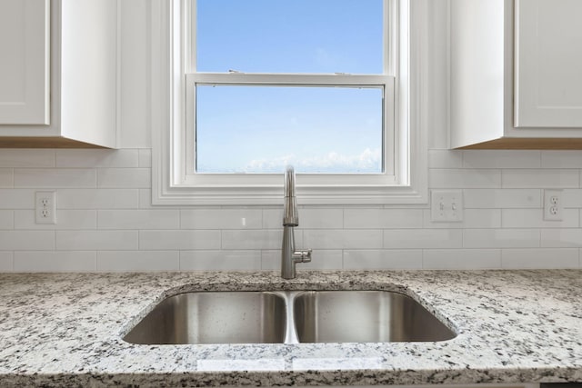 details with white cabinets, backsplash, light stone counters, and sink