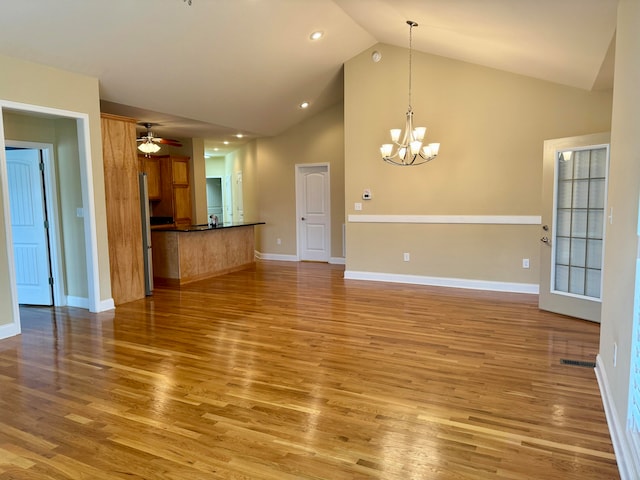 unfurnished living room featuring ceiling fan with notable chandelier, vaulted ceiling, and wood-type flooring