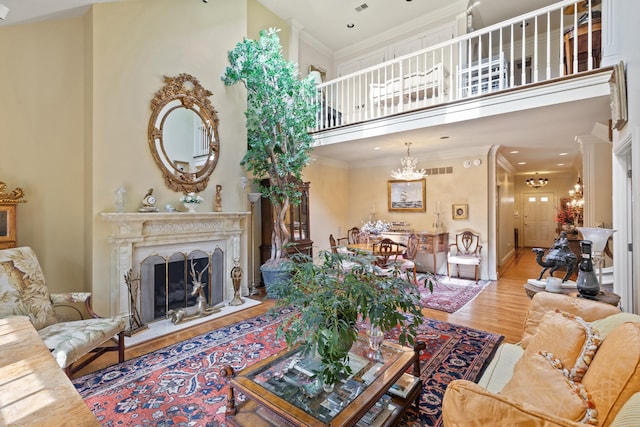 living room featuring crown molding, a high end fireplace, an inviting chandelier, a high ceiling, and wood-type flooring