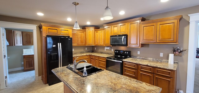 kitchen with sink, light stone counters, hanging light fixtures, an island with sink, and black appliances