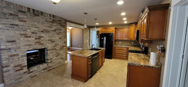 kitchen with pendant lighting, sink, black appliances, a brick fireplace, and a center island with sink