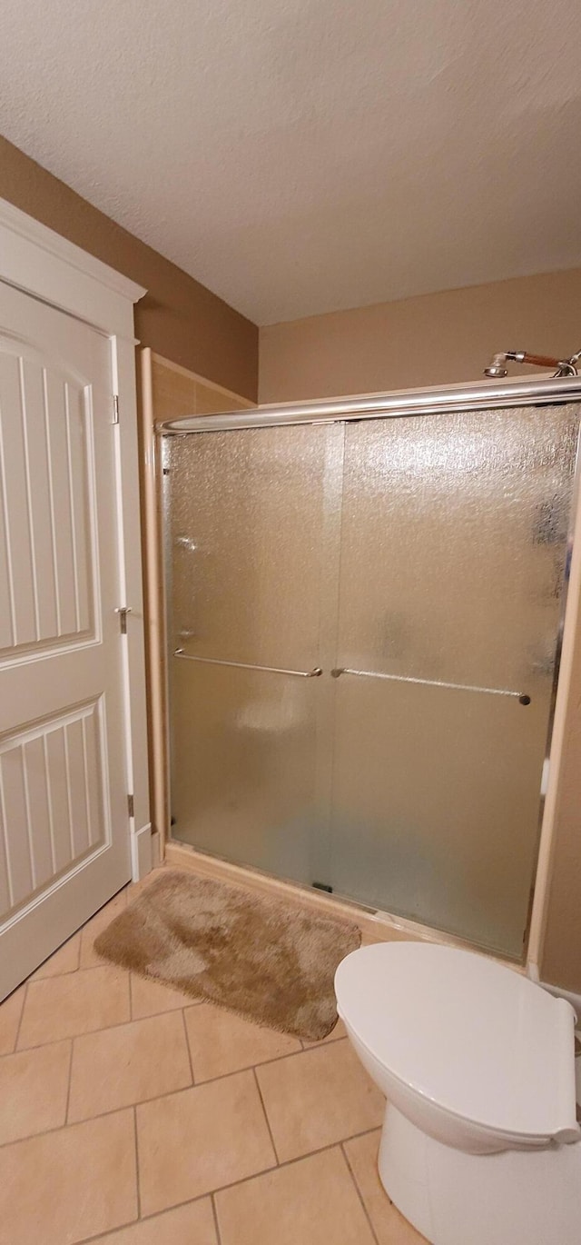 bathroom featuring tile patterned flooring, a shower with door, and toilet