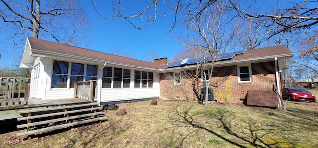 rear view of property with a wooden deck, a lawn, a sunroom, and solar panels