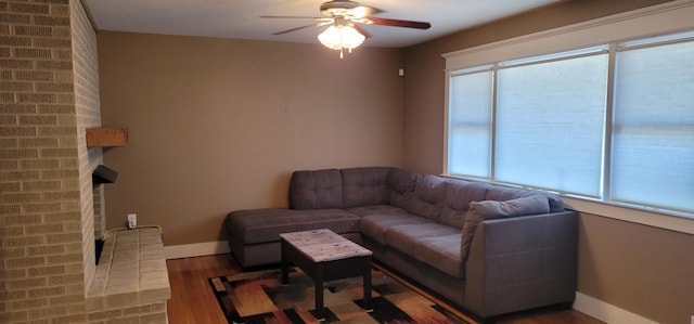 living room featuring a brick fireplace, wood-type flooring, and ceiling fan