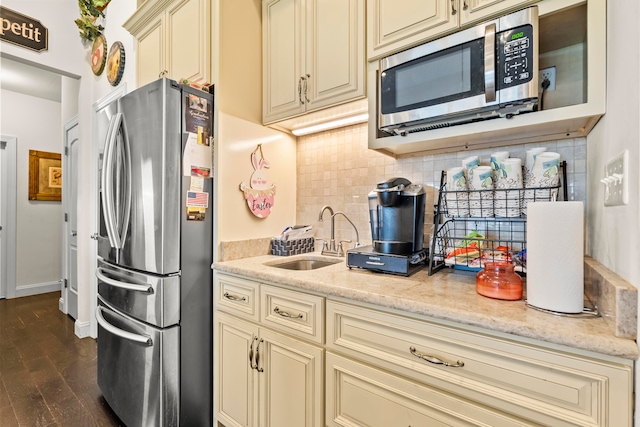 kitchen featuring cream cabinetry, dark wood-type flooring, appliances with stainless steel finishes, backsplash, and sink