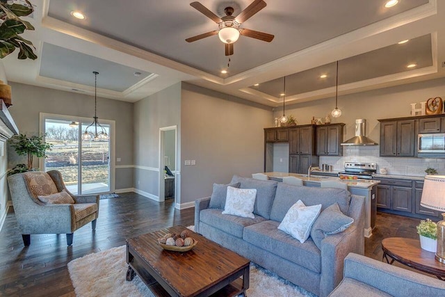 living room featuring a high ceiling, a tray ceiling, dark wood-type flooring, and ceiling fan with notable chandelier