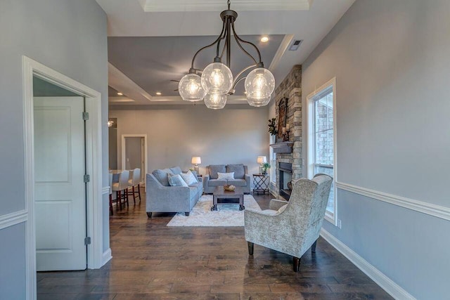 living room featuring a stone fireplace, a notable chandelier, dark hardwood / wood-style floors, and a raised ceiling