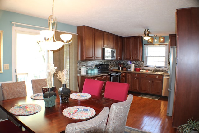 kitchen with sink, dark hardwood / wood-style flooring, stainless steel appliances, tasteful backsplash, and ceiling fan with notable chandelier