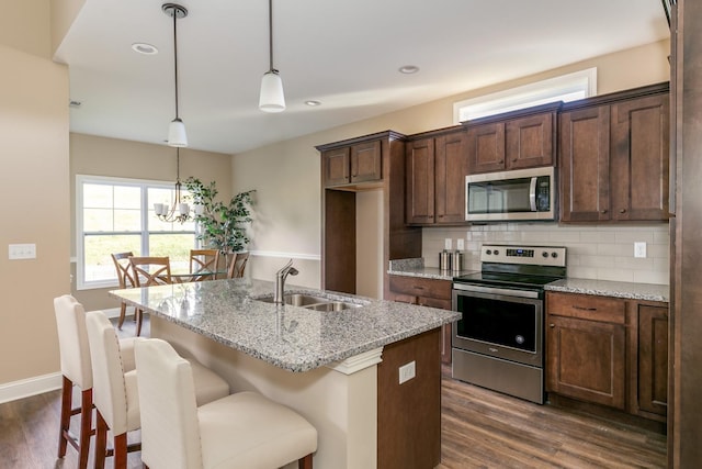 kitchen with stainless steel appliances, light stone countertops, dark wood-type flooring, sink, and an inviting chandelier