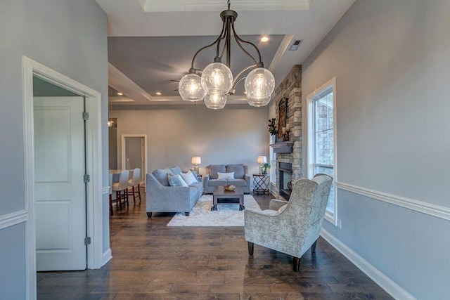 living room featuring a raised ceiling, dark hardwood / wood-style flooring, a chandelier, and a stone fireplace