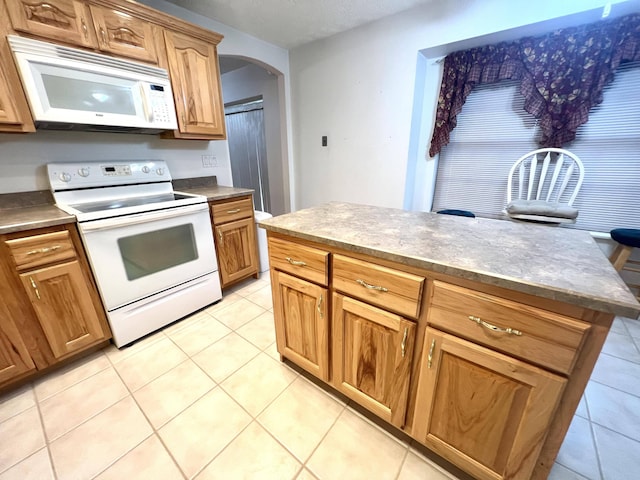 kitchen featuring a textured ceiling, a center island, light tile patterned floors, and white appliances