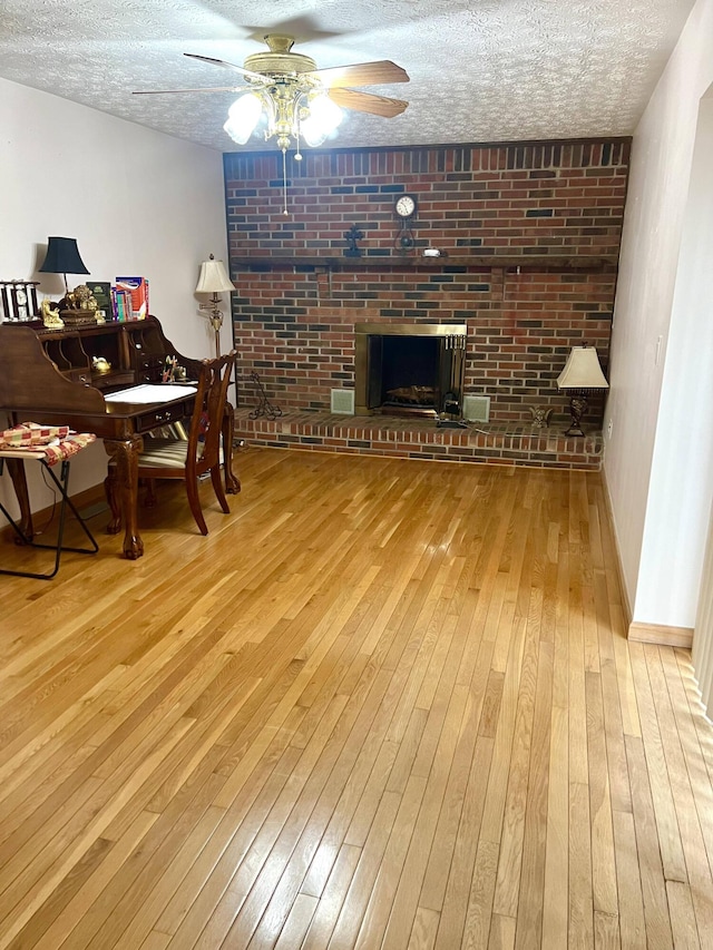 dining room featuring a brick fireplace, a textured ceiling, light hardwood / wood-style flooring, and ceiling fan