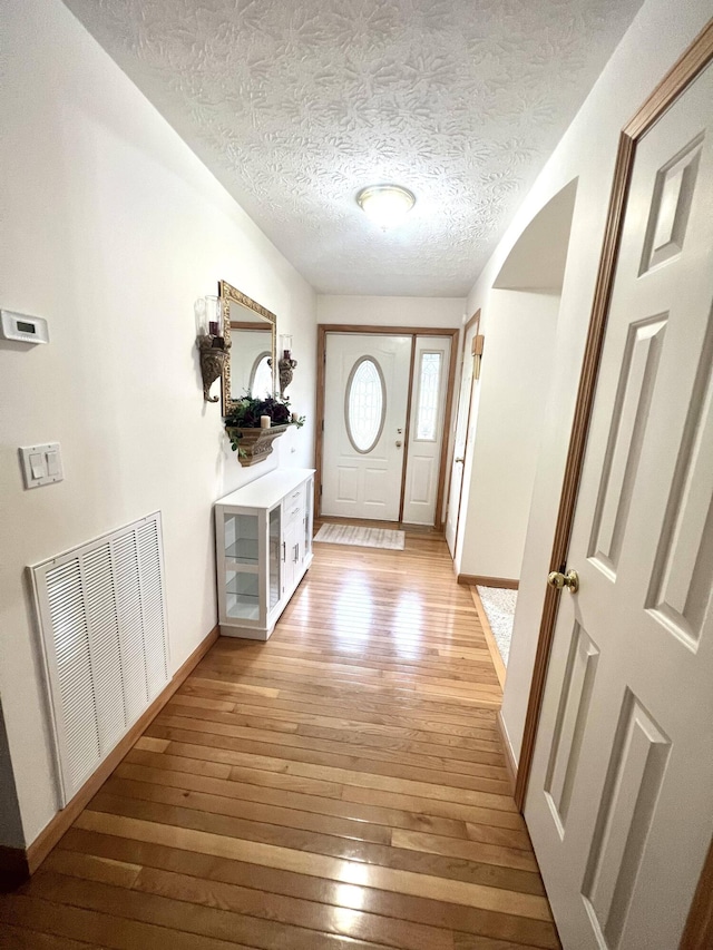 doorway with light hardwood / wood-style floors and a textured ceiling