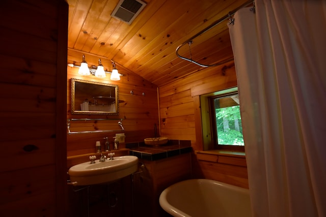 bathroom with a washtub, sink, wooden ceiling, vaulted ceiling, and wooden walls