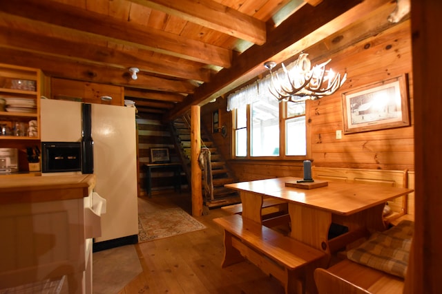 dining space with wooden walls, a notable chandelier, beam ceiling, and wood-type flooring