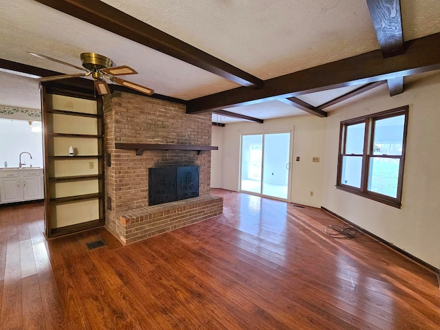 unfurnished living room featuring ceiling fan, a fireplace, a textured ceiling, beam ceiling, and dark hardwood / wood-style flooring