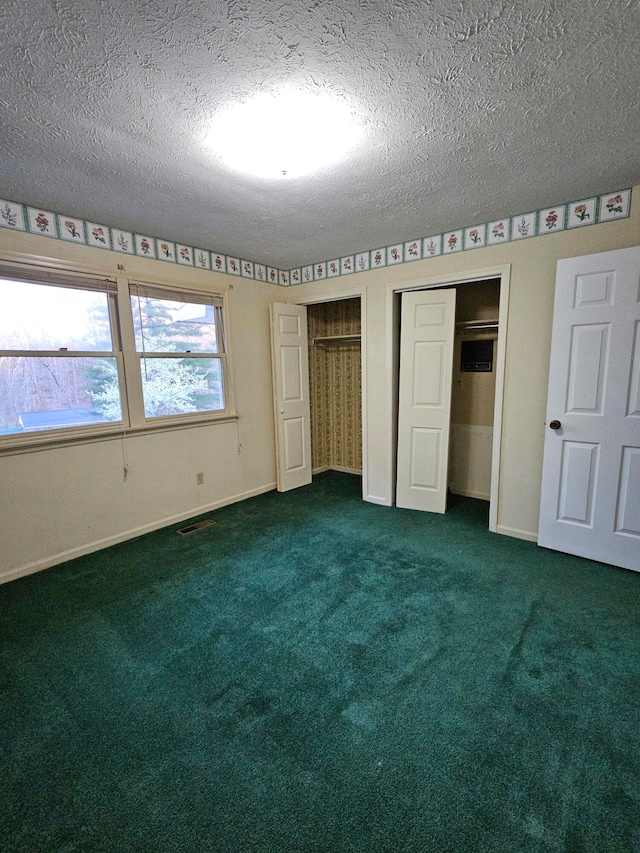 unfurnished bedroom with dark carpet, two closets, and a textured ceiling