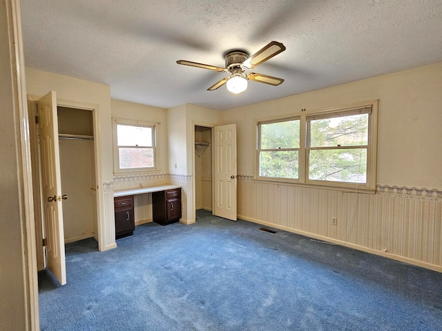 unfurnished bedroom featuring multiple closets, a textured ceiling, dark colored carpet, and ceiling fan