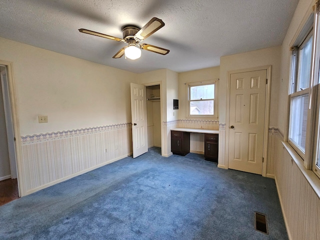 unfurnished bedroom with ensuite bathroom, ceiling fan, dark colored carpet, and a textured ceiling