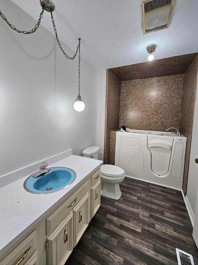 bathroom with toilet, a textured ceiling, wood-type flooring, and vanity