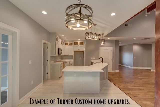 kitchen with an island with sink, white cabinets, hanging light fixtures, light wood-type flooring, and sink