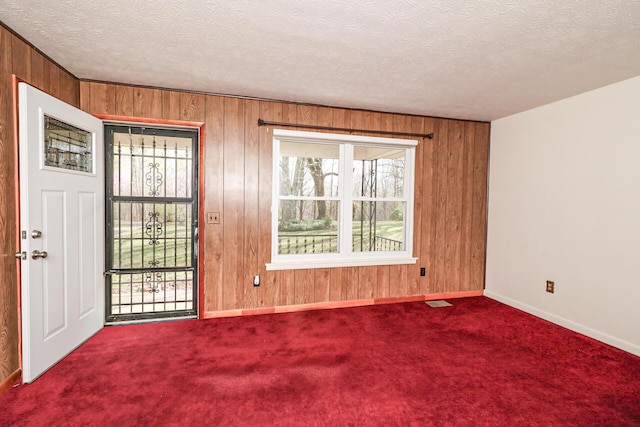 empty room featuring wood walls, a textured ceiling, and carpet flooring