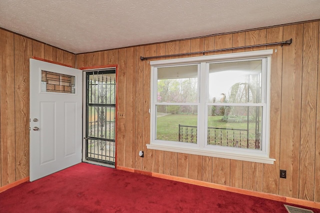 interior space with a textured ceiling, plenty of natural light, visible vents, and wooden walls