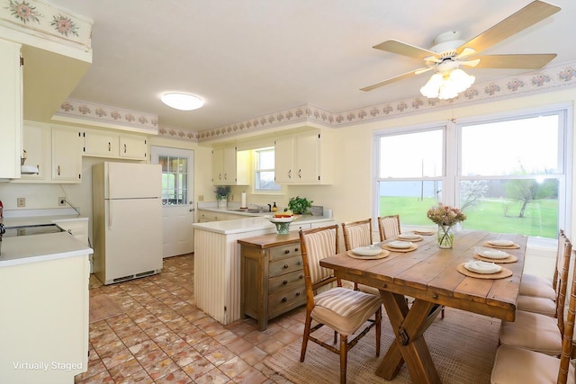 kitchen featuring ceiling fan, a peninsula, a sink, light countertops, and freestanding refrigerator