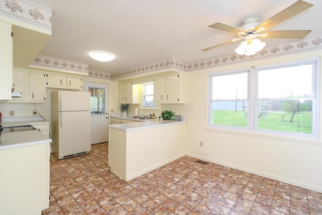 kitchen featuring light countertops, freestanding refrigerator, a sink, a peninsula, and baseboards