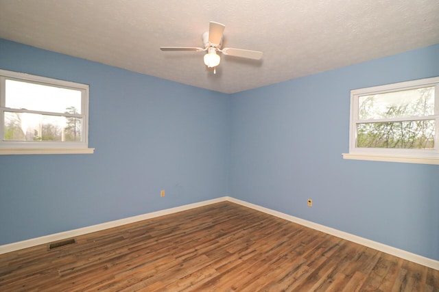 empty room featuring baseboards, plenty of natural light, visible vents, and wood finished floors