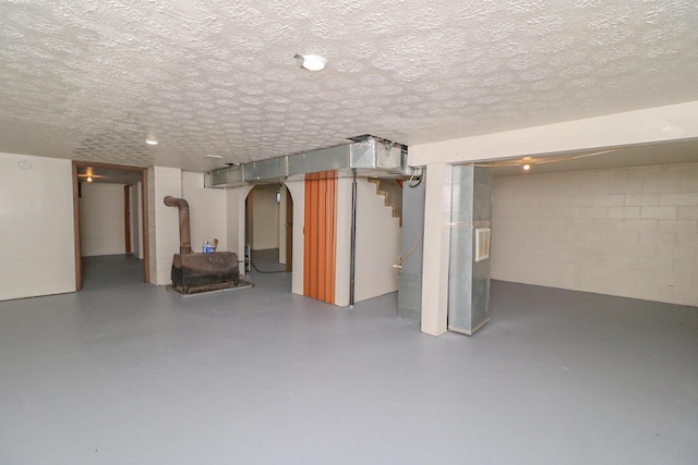 finished basement with a textured ceiling, arched walkways, and concrete block wall