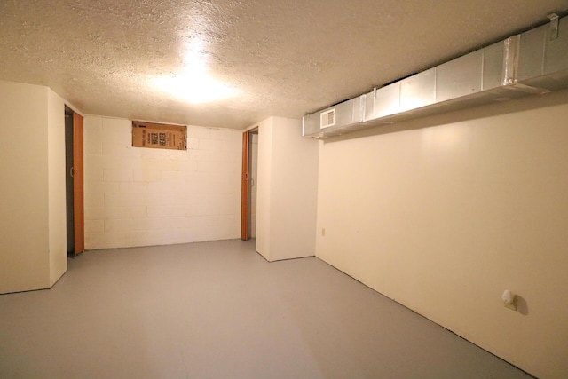 finished below grade area with concrete block wall, visible vents, and a textured ceiling