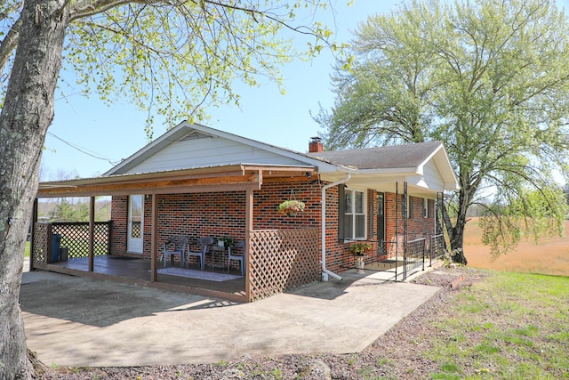 view of front of home with a porch, brick siding, and a chimney