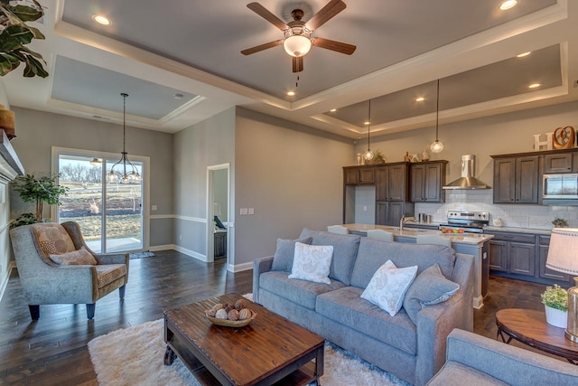 living room featuring dark hardwood / wood-style flooring, ceiling fan with notable chandelier, and a tray ceiling