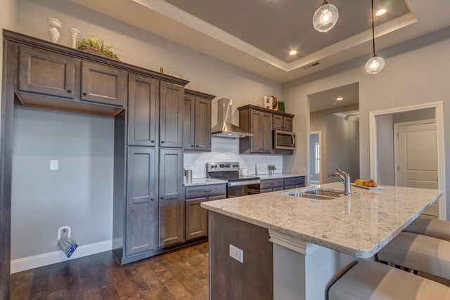 kitchen featuring pendant lighting, light stone counters, stainless steel appliances, wall chimney exhaust hood, and a tray ceiling