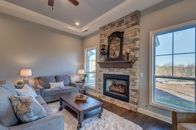 living room featuring dark hardwood / wood-style flooring, ceiling fan, a stone fireplace, and a tray ceiling