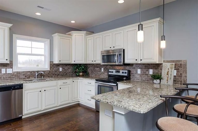 kitchen with appliances with stainless steel finishes, a kitchen breakfast bar, white cabinets, and decorative light fixtures