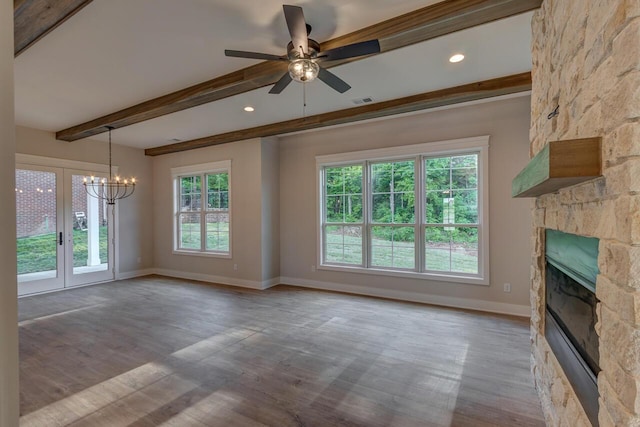 unfurnished living room with ceiling fan with notable chandelier, french doors, beamed ceiling, a stone fireplace, and light hardwood / wood-style flooring