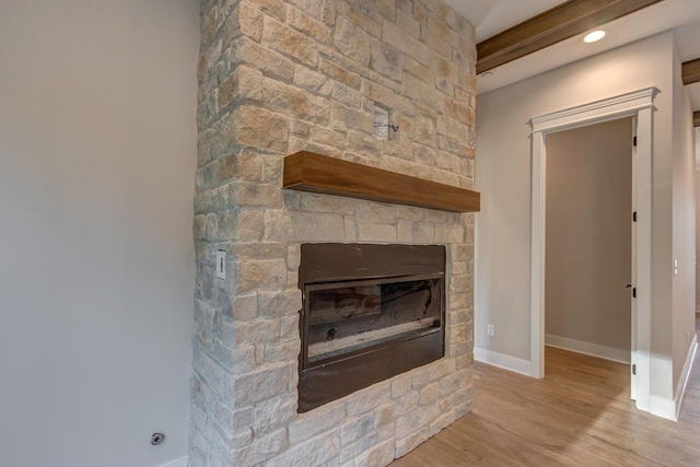 details with beam ceiling, wood-type flooring, and a stone fireplace