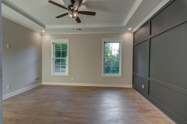 empty room featuring a raised ceiling, ceiling fan, crown molding, and light hardwood / wood-style floors