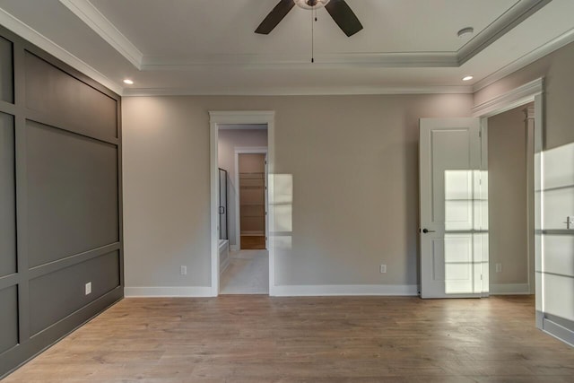 unfurnished bedroom featuring a raised ceiling, ceiling fan, light wood-type flooring, and crown molding