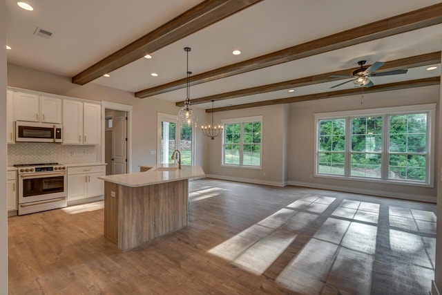 kitchen featuring tasteful backsplash, a center island with sink, stove, beamed ceiling, and white cabinets