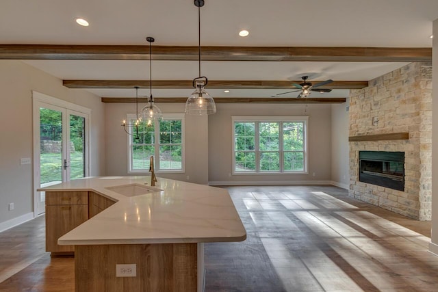 kitchen featuring decorative light fixtures, beamed ceiling, a fireplace, sink, and a kitchen island with sink