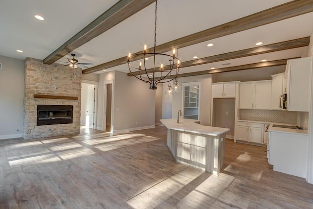 kitchen featuring white cabinetry, decorative backsplash, a kitchen island with sink, a fireplace, and beam ceiling