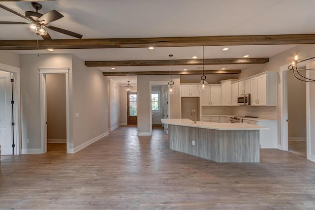 kitchen with an island with sink, stainless steel appliances, decorative backsplash, white cabinets, and beamed ceiling