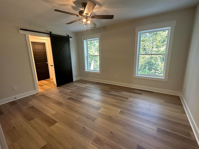 unfurnished bedroom featuring multiple windows, hardwood / wood-style floors, a barn door, and ceiling fan