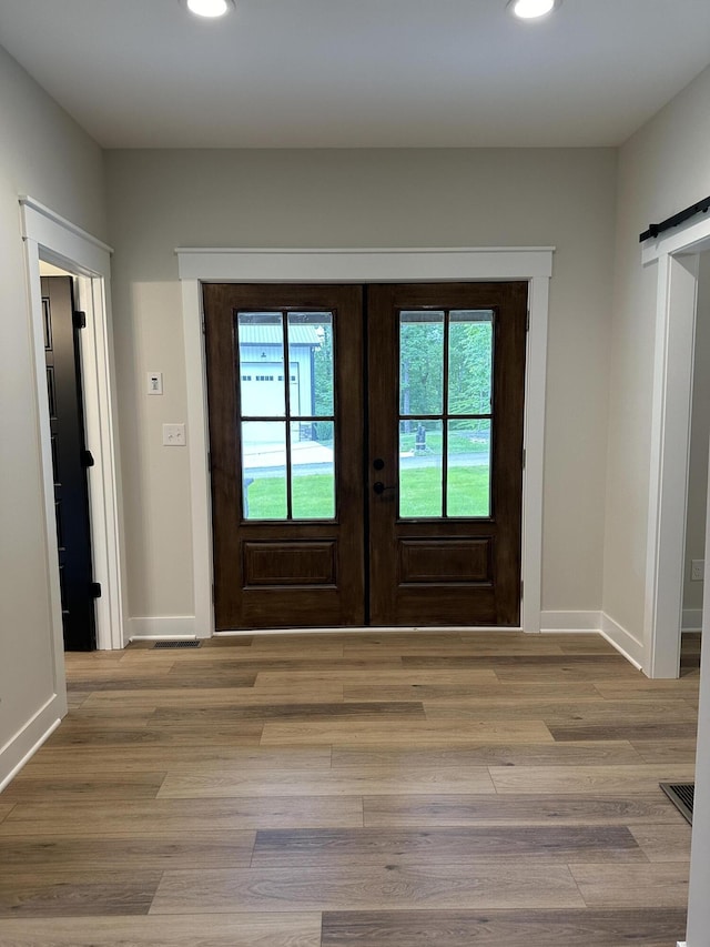 entryway featuring a barn door, french doors, and light hardwood / wood-style flooring