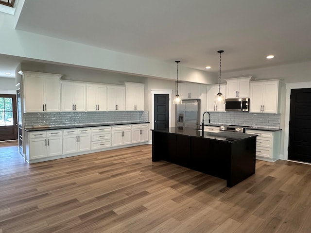 kitchen with stainless steel appliances, sink, decorative light fixtures, a center island with sink, and white cabinetry