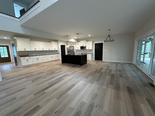 kitchen with white cabinetry, a kitchen island with sink, decorative light fixtures, decorative backsplash, and appliances with stainless steel finishes