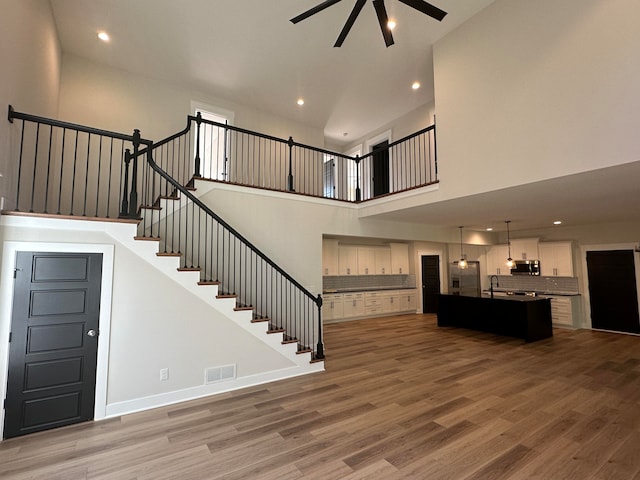 unfurnished living room featuring hardwood / wood-style floors, ceiling fan, sink, and a high ceiling